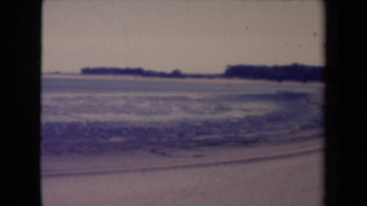 Soft-focus waves and sand with a distant low shoreline under a muted sky.