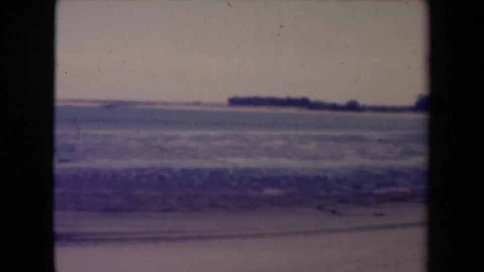 France 1945 8mm frame showing surf near the beach and a dark, low shoreline in the distance.