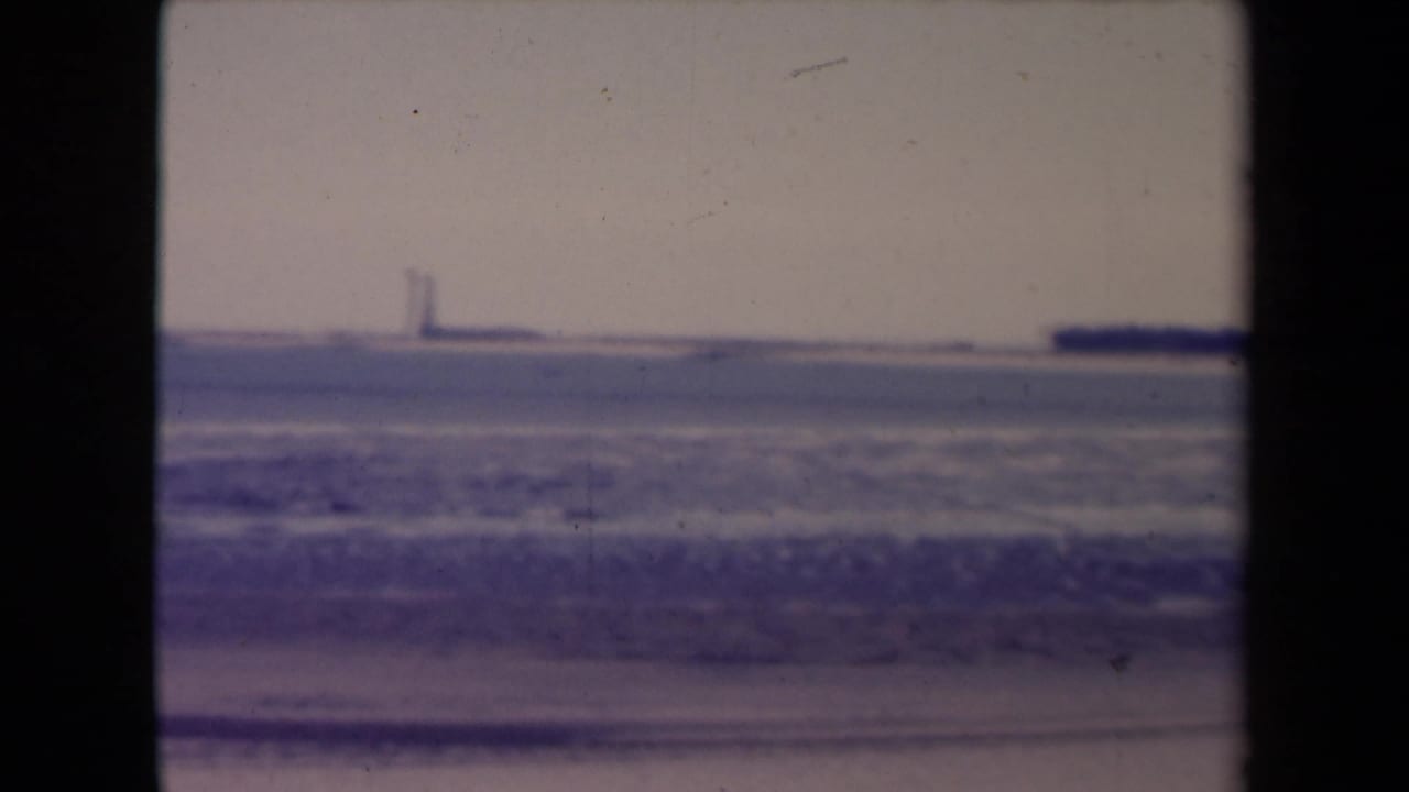 Snowy open landscape with a distant vertical structure and dark 8mm frame borders.