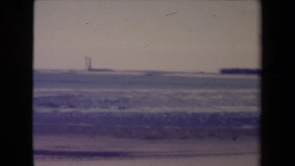 Archival 8mm view of a pale snowy expanse in France, with a distant vertical shape on the horizon and heavy film-frame borders.