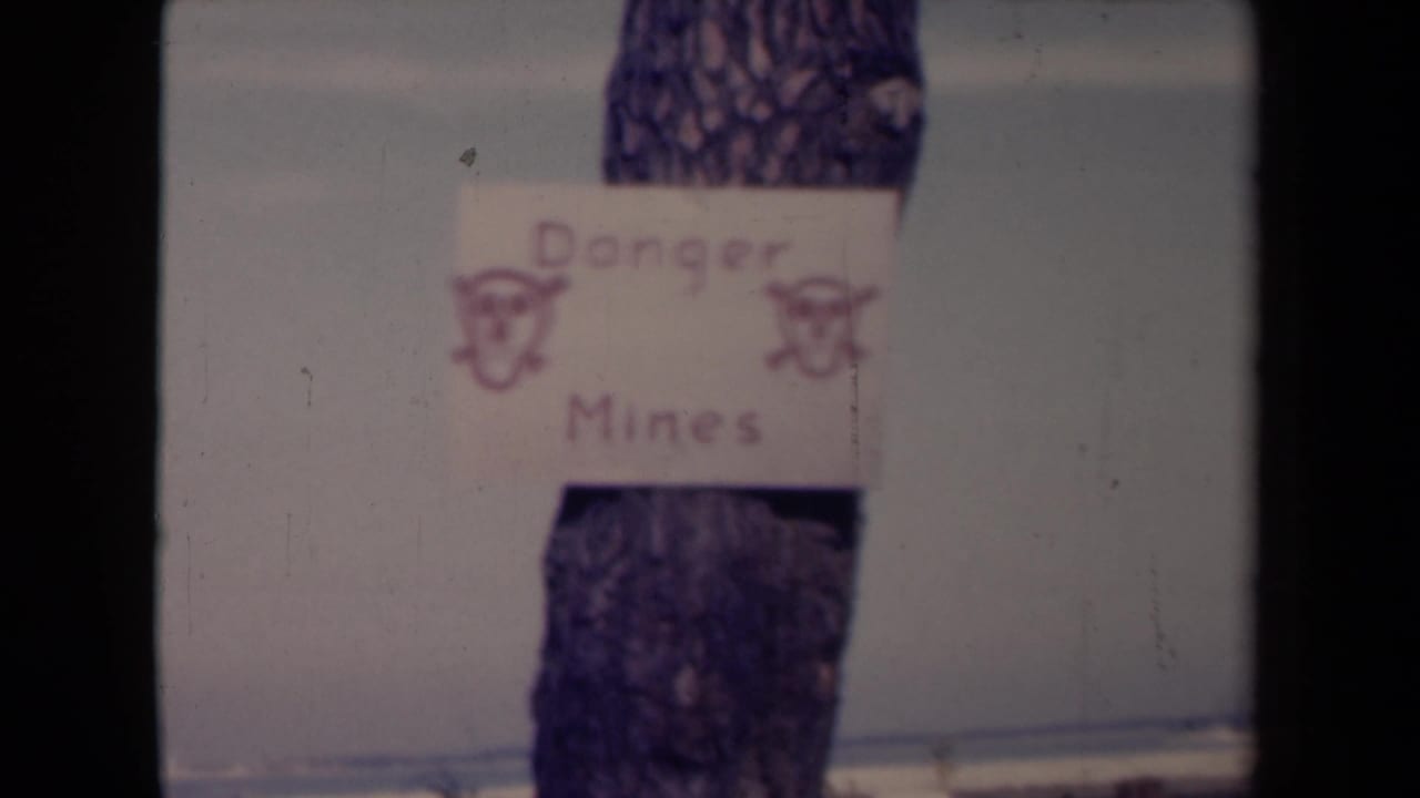 Hand-drawn Danger Mines sign attached to a tree trunk against pale snowy ground.