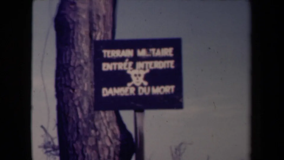 1945 France 8mm frame showing a blue restricted military zone sign mounted beside a tree in a quiet wooded area.