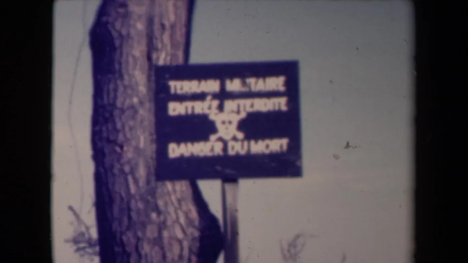 1945 France 8mm frame of a French military land warning sign, slightly soft and framed by a tree trunk.