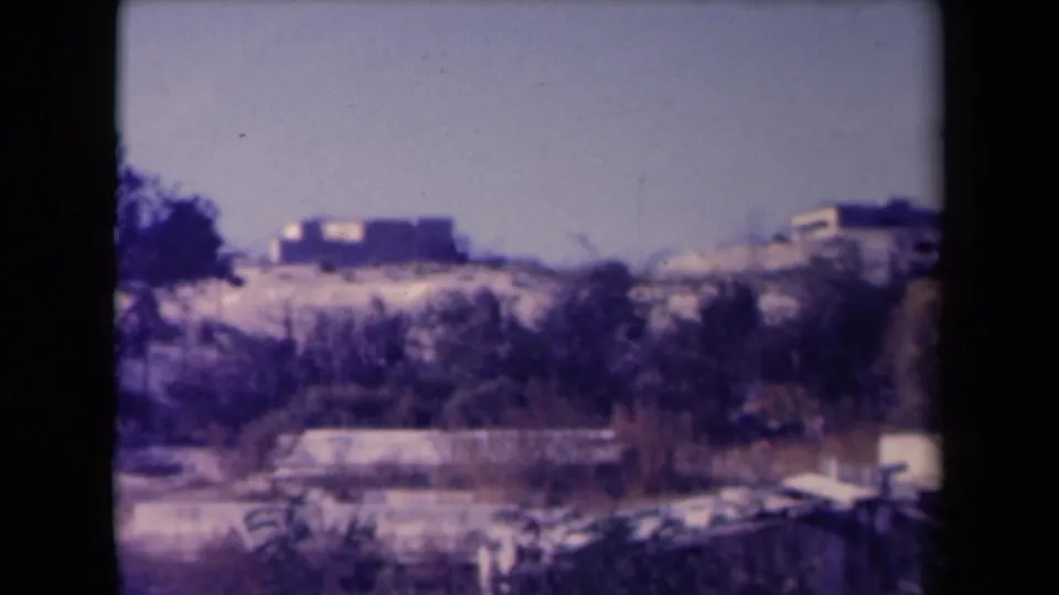 1945 France 8mm frame showing sandy hills with distant low homes, sparse trees, and a dark foreground edge.