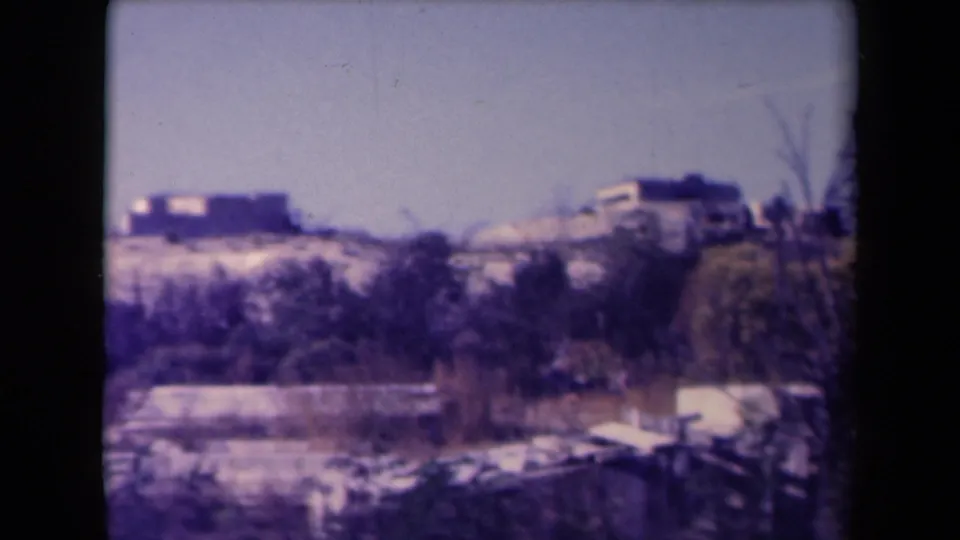 1945 France home-movie view of a sandy hillside settlement seen past brush and low foreground structures.