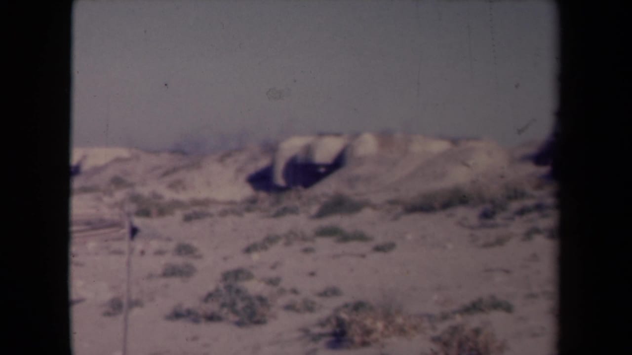 Barren sandy ground with sparse scrub beneath a pale sky.
