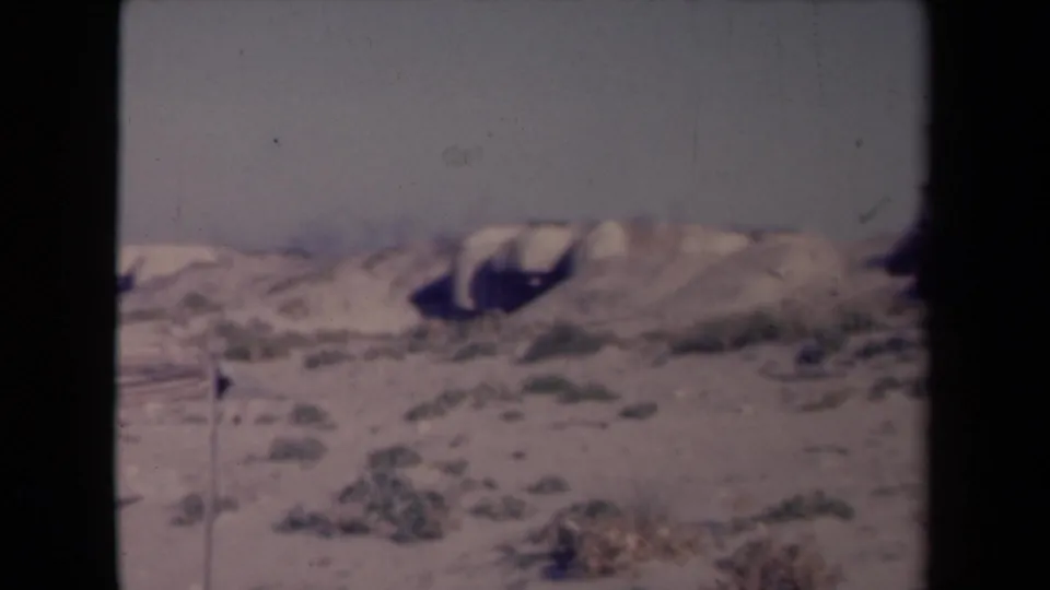 Metadata-identified 1945 France 8mm frame showing sandy ridges, scattered low vegetation, and a soft pale horizon.
