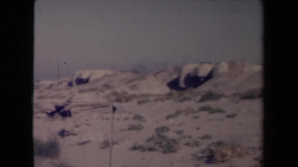 Metadata-identified 1945 France 8mm frame with pale sky, sand, scrub patches, and soft focus from the camera pan.