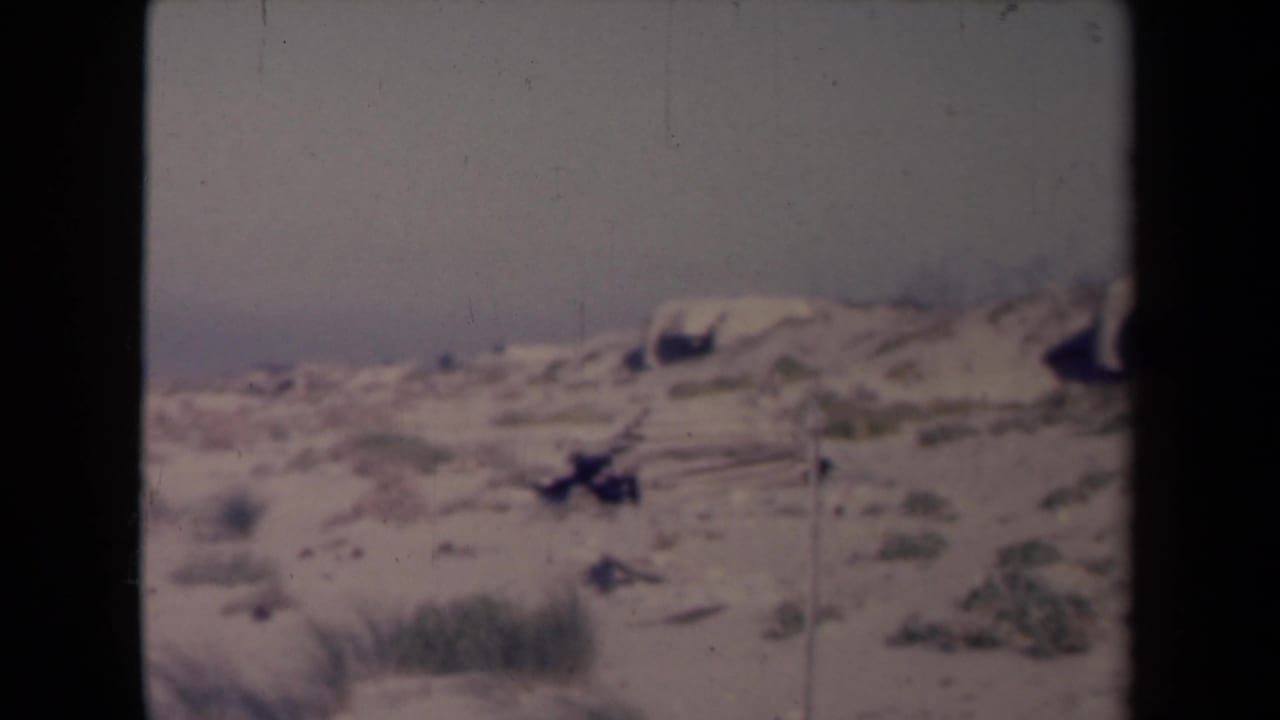 Metadata-identified 1945 France 8mm frame with open sand, scattered scrub, pale sky, and a visible film-strip edge.
