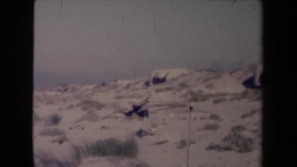Metadata-identified 1945 France 8mm frame with open sand, scattered scrub, pale sky, and a visible film-strip edge.
