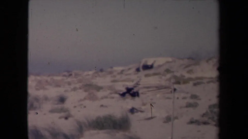 1945 France 8mm frame showing sandy coastal dunes, sparse vegetation, and a hazy sky with no people visible.