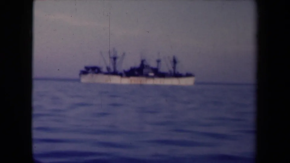1945 France 8mm frame showing a distant large vessel on calm blue sea, silhouetted against a hazy horizon.