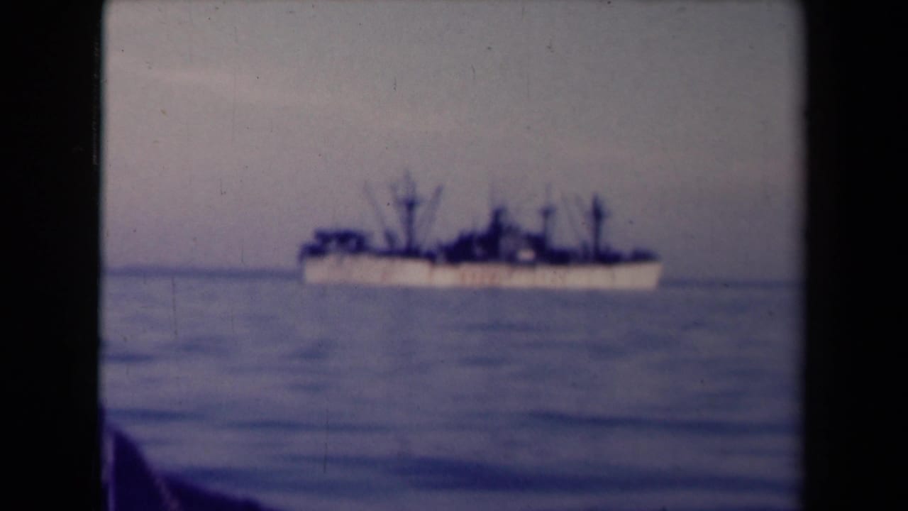 Soft 8mm frame of a large ship at sea in France, with visible grain, faded color, and a dark foreground shape at lower left.
