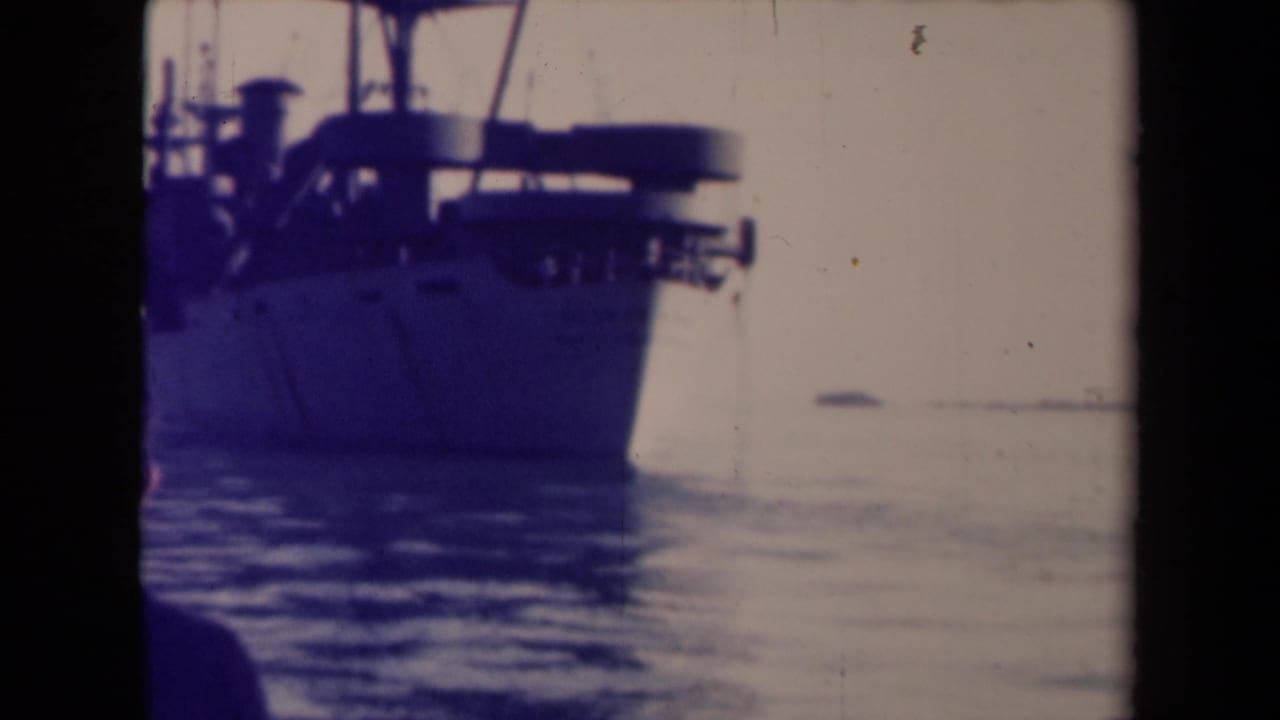 1945 France 8mm frame with a closer partial ship view, calm water, pale sky, and an indistinct observer silhouette in the foreground.