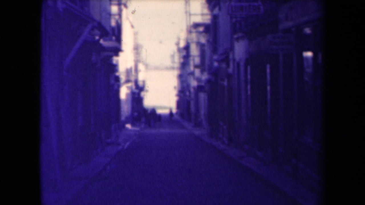 1945 France home-movie view down a narrow village street lined with buildings and distant pedestrians.