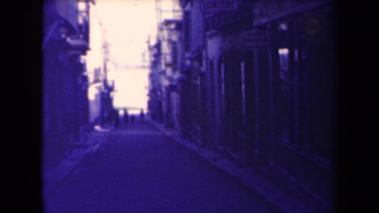 Narrow street between buildings with distant pedestrians and strong blue-purple film tint.