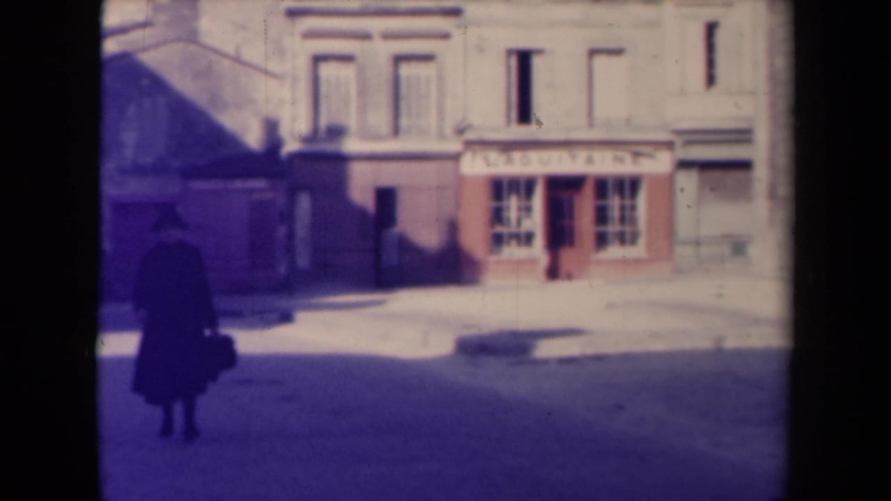 Man in a dark coat walks across a quiet street near a small shop and large stone building.