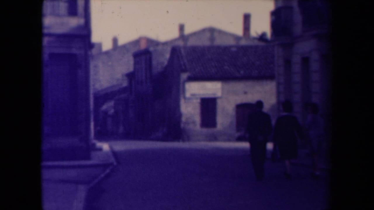 Pedestrians walk away along a narrow street between old buildings.