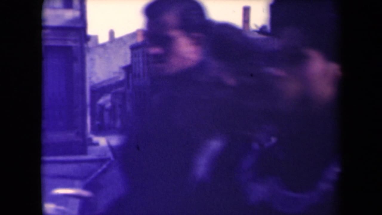 A blurred passerby crosses very near the lens, partially obscuring the French town street and distant pedestrians.