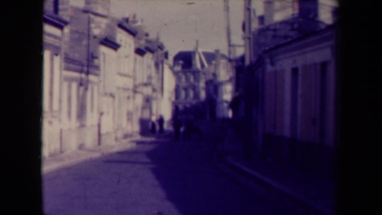 Sunlit building facades along a narrow street with pedestrians in the distance.