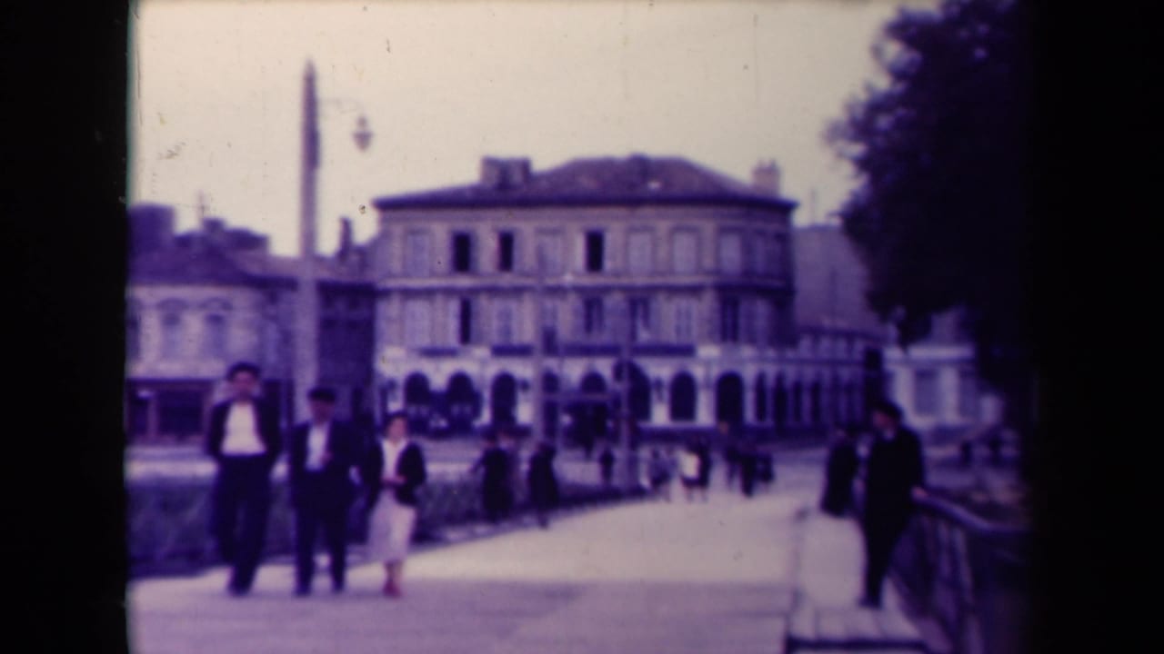Small group walking on a promenade in front of a large arched building.