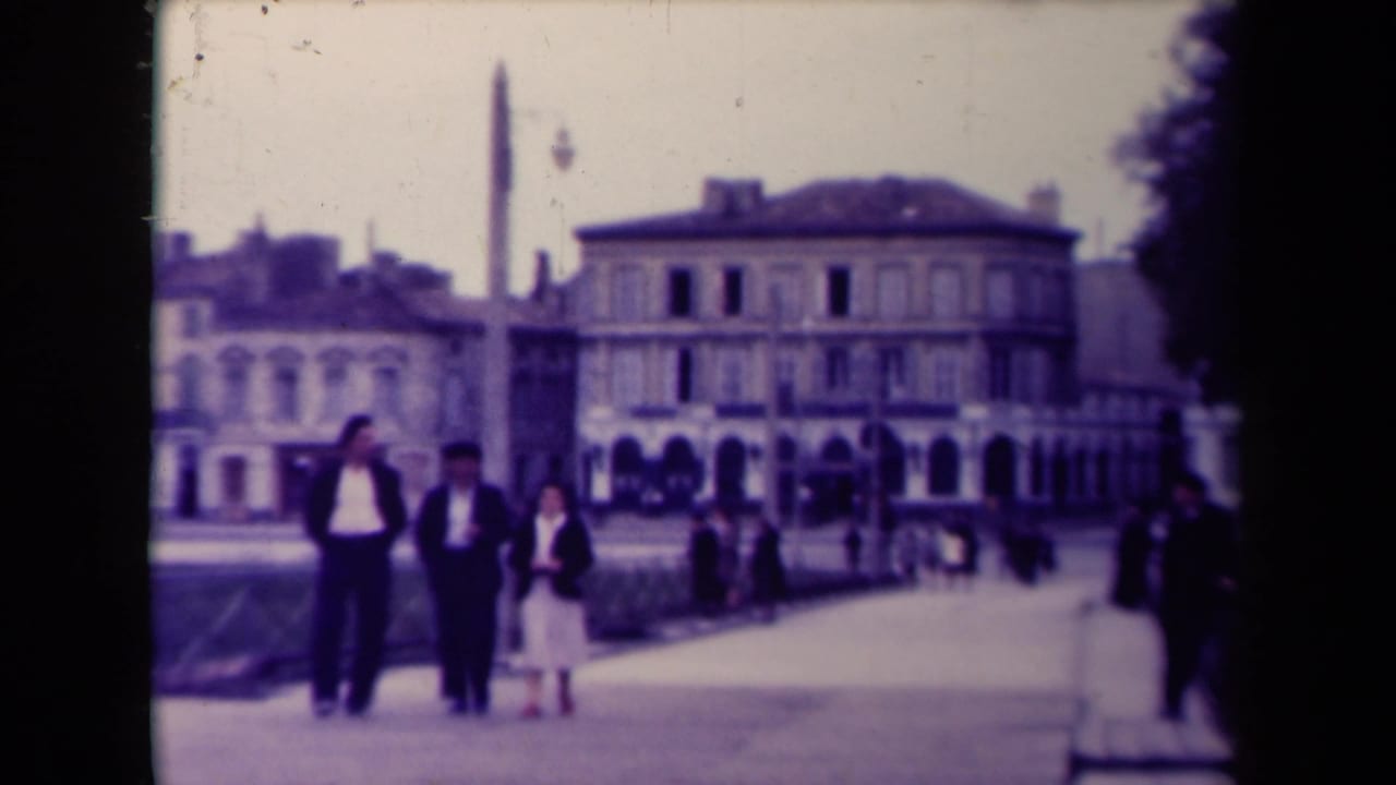 Three people walk toward the camera with a historic building and monument behind them.