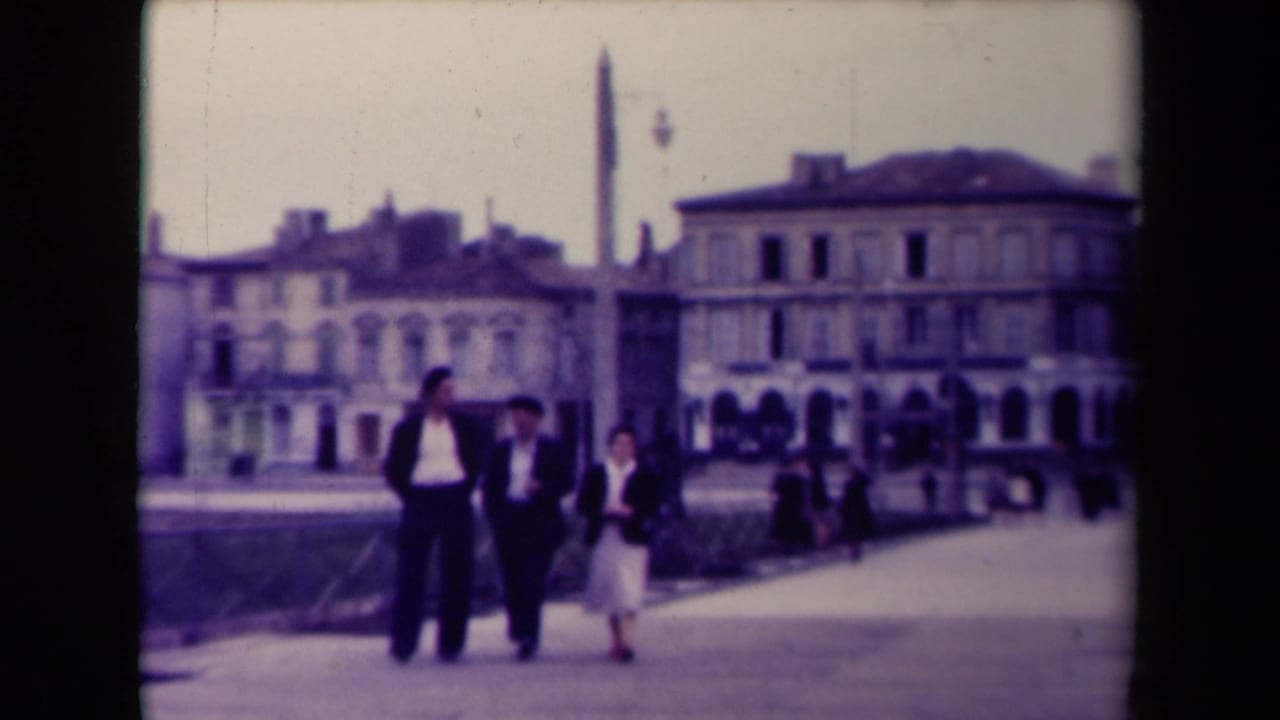 The group moves closer on a French promenade, with railings, background pedestrians, and soft-focus historic buildings visible.