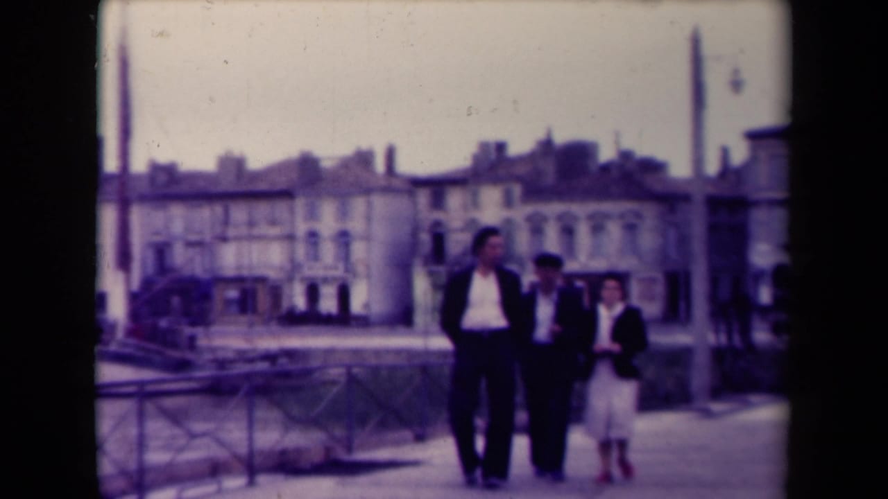 Three people continue walking past railings with water and buildings in the background.