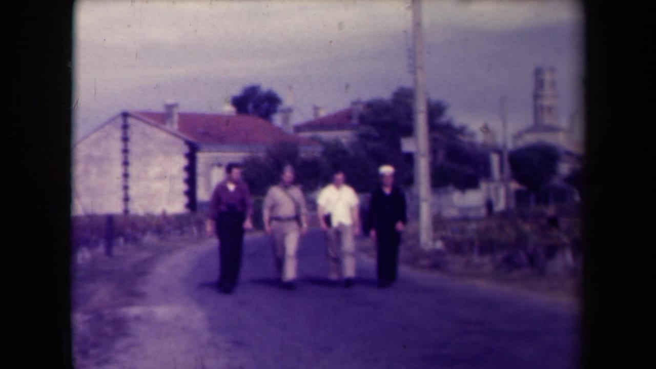 Four men walk toward the camera on a village road with buildings behind them.