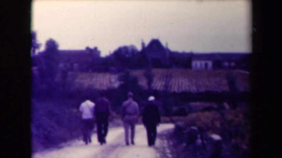 At the end of the clip, the four men walk away along the vineyard road in France, with a church tower and rural buildings silhouetted ahead.