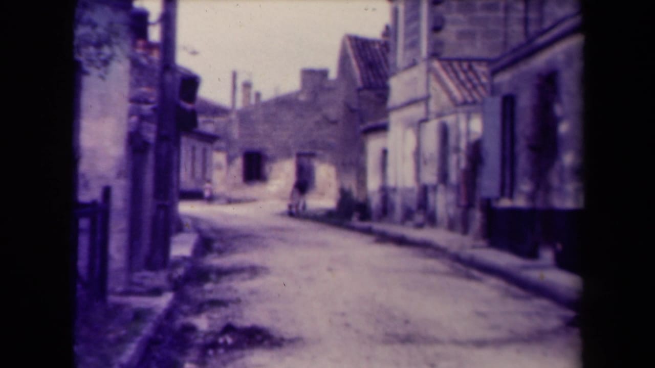 Narrow village street with a lone figure farther down the road carrying an item.