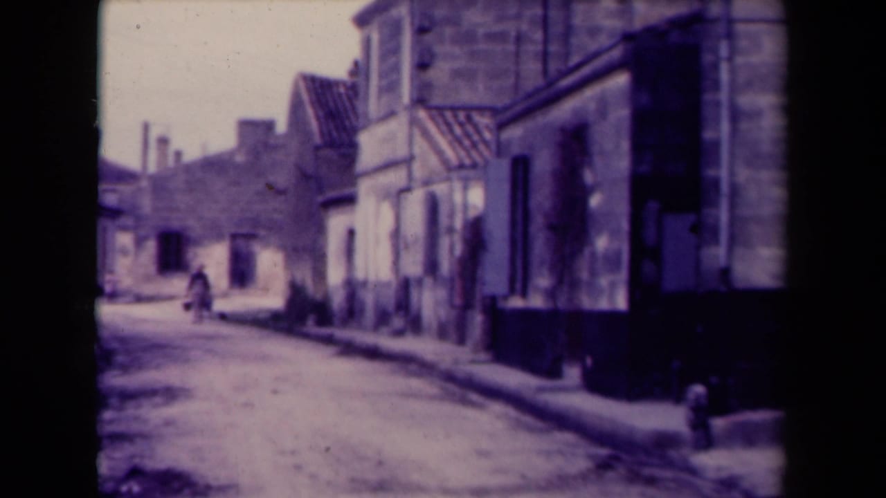 Stone village street with a distant person and low buildings along a pale road.