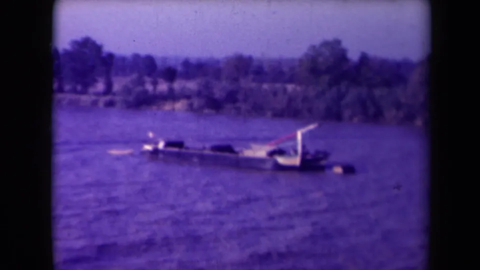 A partially submerged vessel sits in the Gironde River, with water, shoreline, trees, and soft 8mm color visible.