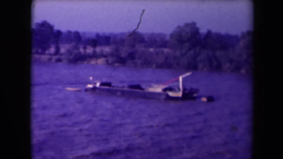 The damaged vessel remains partly above the Gironde River surface, with a wooded bank and film scratches in view.
