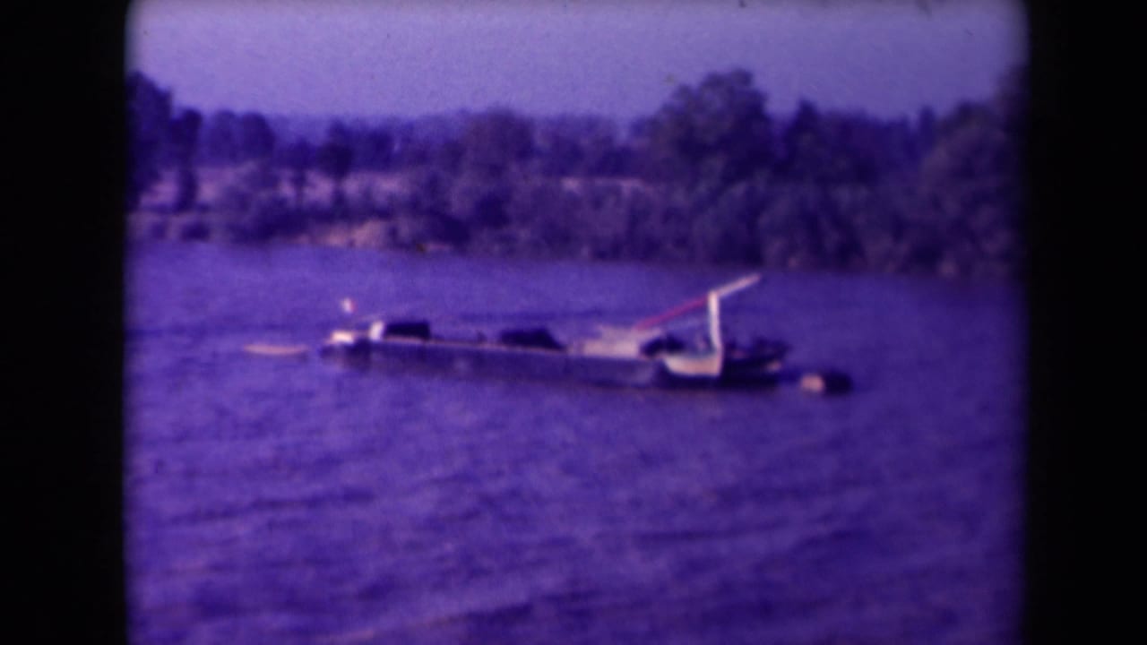 Small vessel or wreckage low in rippled water with distant tree-lined shore.