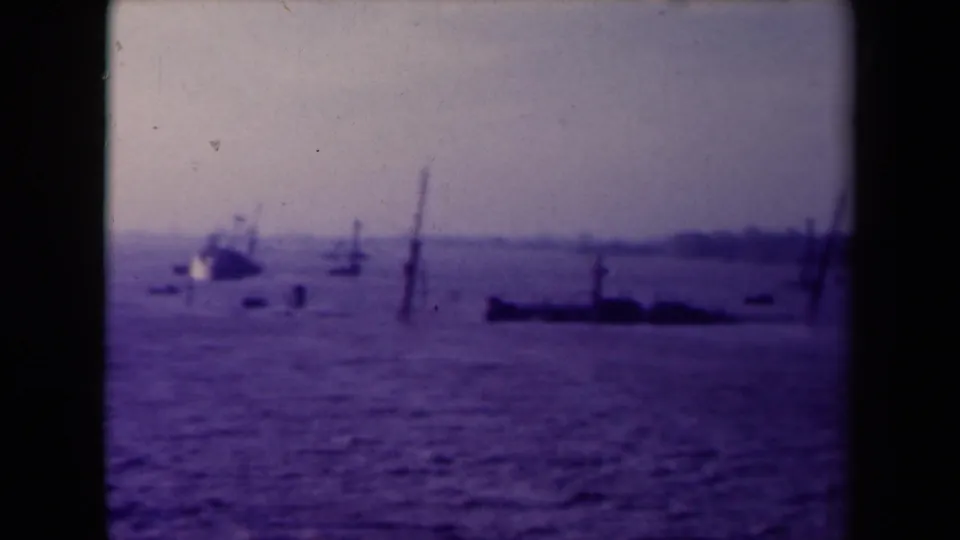 Purple-tinted France 1945 8mm view of a small boat and partially submerged-looking hulls in distant water.