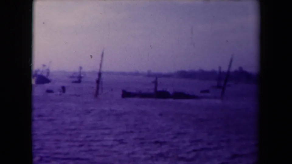France 1945 8mm frame showing a dark low vessel shape, exposed masts, and soft shoreline in purple-blue water.