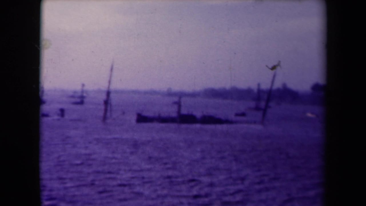 Purple-toned waterfront with submerged posts, small boats, and a distant shoreline.