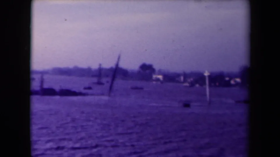 1945 France 8mm frame showing rippled floodwater, distant shore, and a leaning dark marker near the waterline.