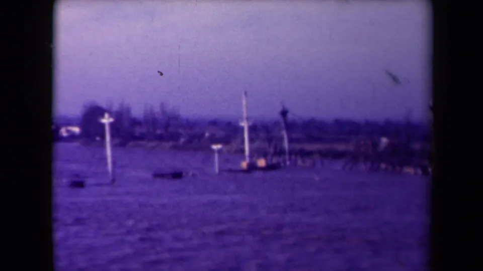 1945 France 8mm frame of several cross-shaped markers standing in floodwater near a hazy shore.