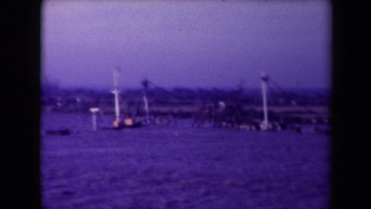 Distant waterfront with tall pale structures, small dark shapes on water, and hazy sky.