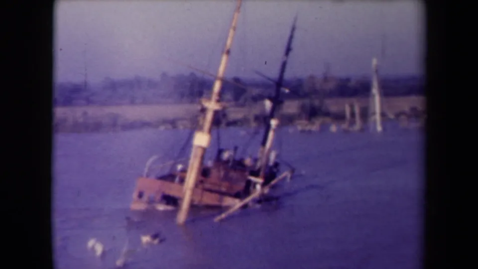 France 1945 8mm frame showing a red and white vessel partly submerged in a river, with masts leaning and a soft distant shore in the background.
