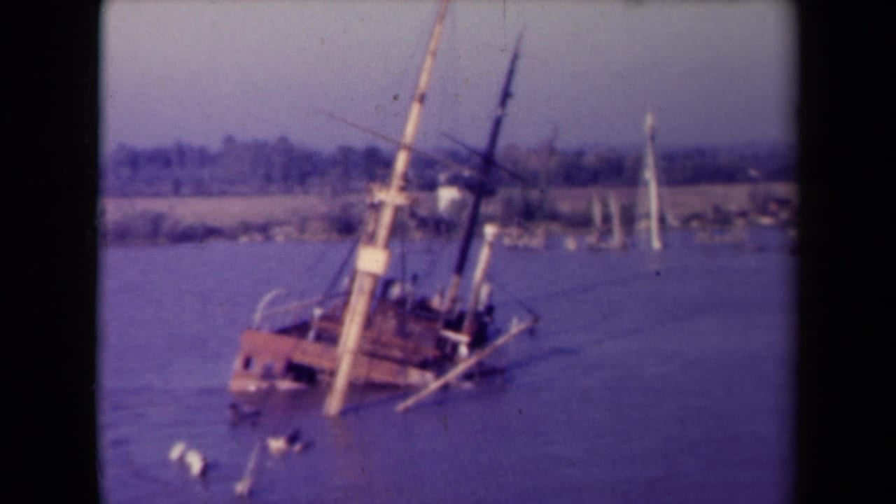 The same tilted vessel sits lower in the water, with rigging angled sharply against a hazy shoreline.