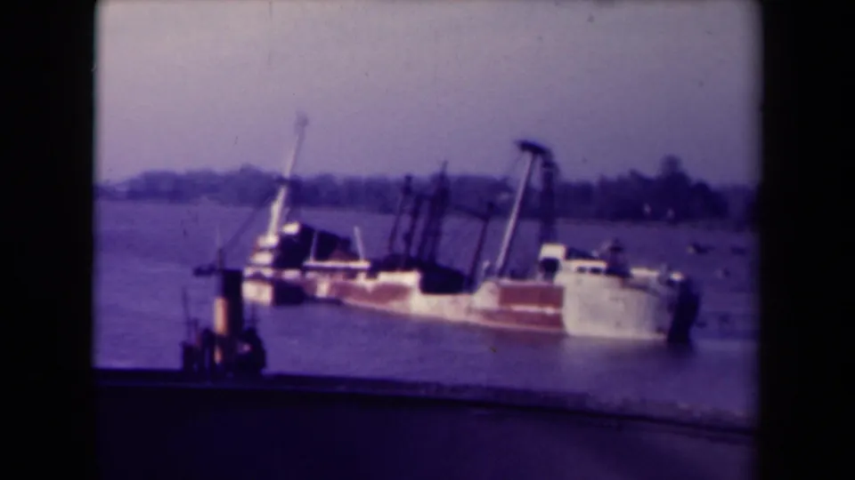 France 1945 8mm frame showing a low red and white vessel in river water, with posts, haze, and an indistinct shoreline beyond.