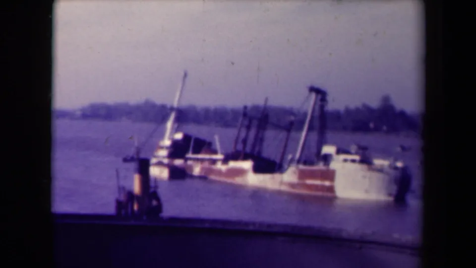 France 1945 8mm frame of the river scene after the vessel has settled lower, with dark posts, a pale stern, and a hazy shore beyond.