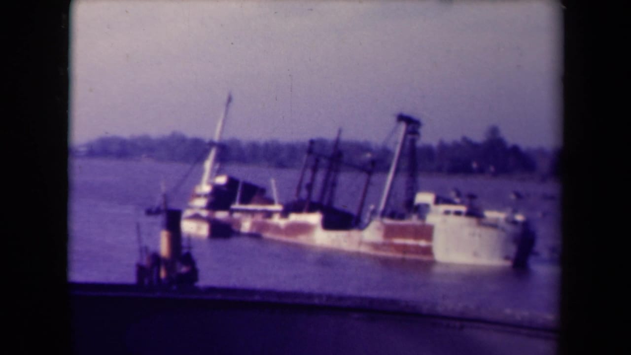 Large vessel listing in calm harbor water near a dock.