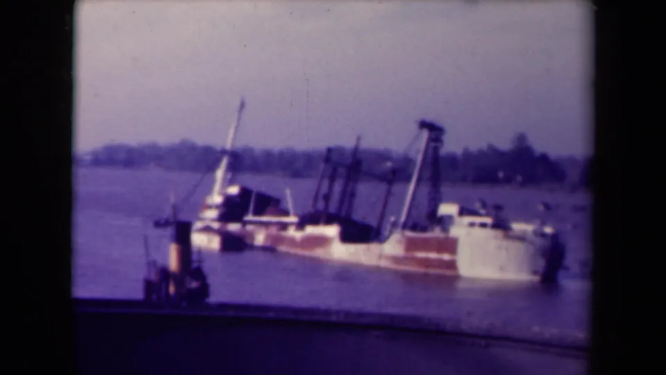 1945 France home-movie frame showing a large weathered vessel leaning heavily in harbor water near dock structures.
