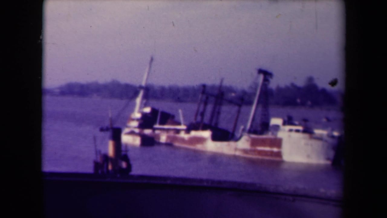 Listing vessel seen from shore with rigging and distant shoreline.