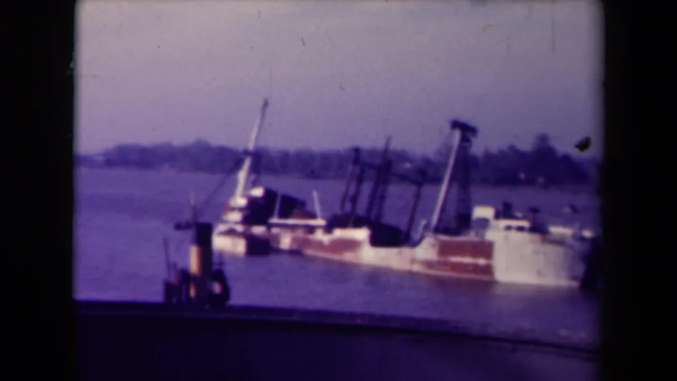1945 France frame of a weathered harbor vessel tilted in the water, with rigging visible against a soft distant shoreline.
