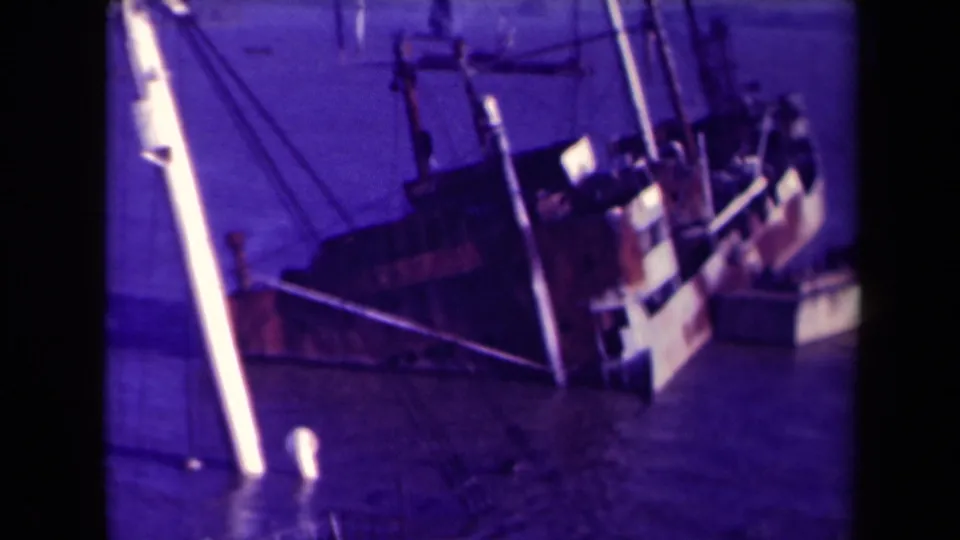 Closer 1945 France view of the distressed vessel, with its hull low in the water and rigging crossing the frame near dock posts.